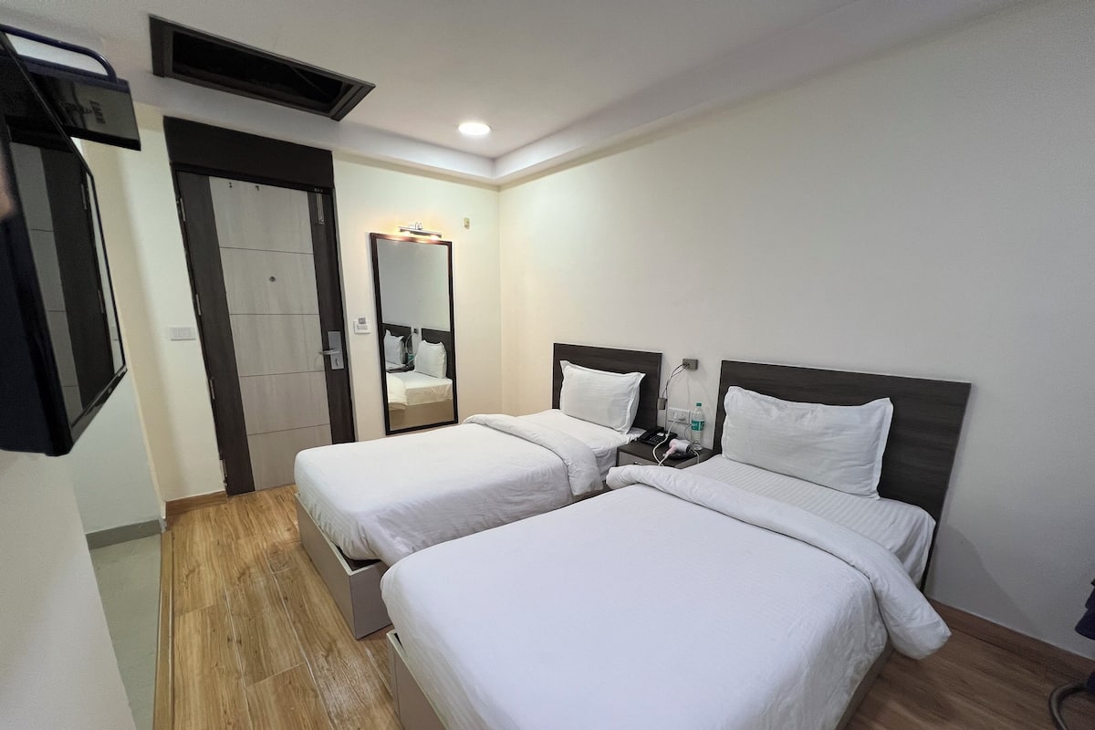 A hotel room with two beds, a mirror, a nightstand with a phone and a bottle, and a wooden floor.