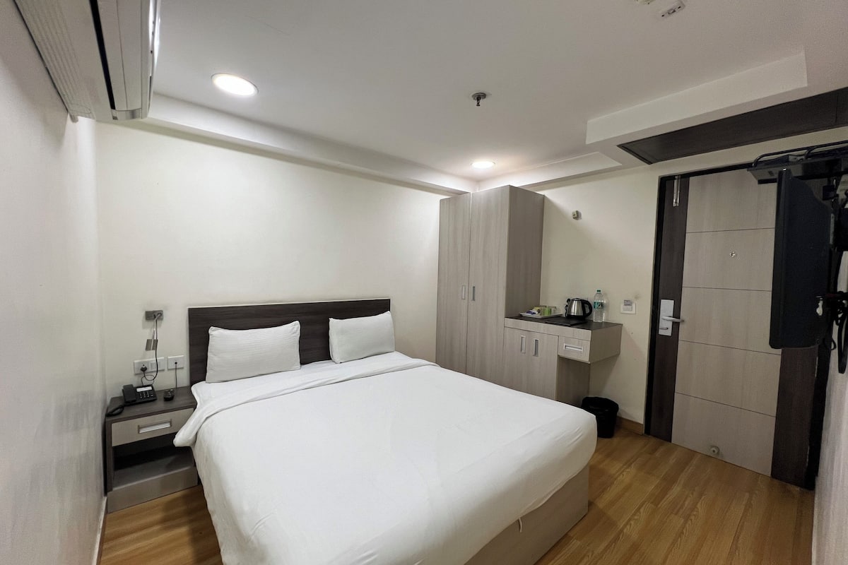 A hotel room with a bed, a nightstand, a wardrobe, and a small kitchenette area.