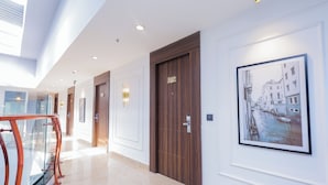 A hotel corridor with wooden doors, framed artwork, and a glass railing. - Hyphen Business Hotel (Noida)