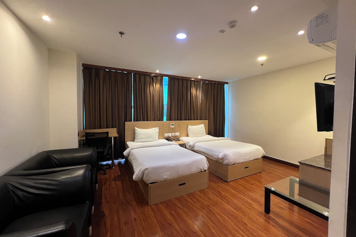 A hotel room with two beds, a desk, a chair, and a TV.