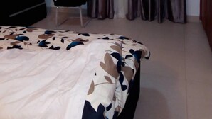 A bedroom with a bed, a TV on a stand, a chair, and a wardrobe. - Reeve Court Apartment (Lagos)