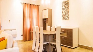 A dining area with a table and chairs, a sofa, a cabinet, and a decorative wall piece. - Reeve Court Apartment (Lagos)