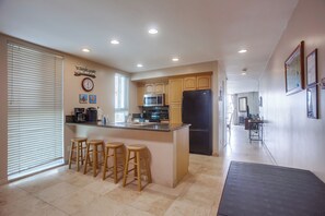 A kitchen with a central island, bar stools, a microwave, a refrigerator, and a clock on the wall.