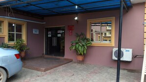 A building entrance with a blue awning, a car parked in front, and a potted plant beside the entrance. - Richanthonio Suites (Lagos)