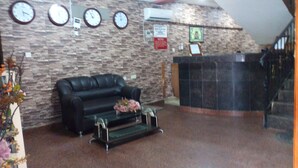 A lobby with a stone wall, a black leather sofa, a reception desk, and three clocks on the wall. - Richanthonio Suites (Lagos)