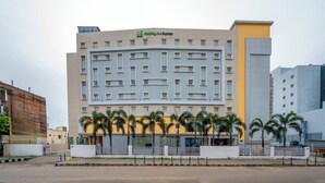 A Holiday Inn Express building with a modern design, featuring a central courtyard with palm trees. - Holiday Inn Express Chennai OMR Thoraipakkam by IHG (Chennai)