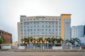 A Holiday Inn Express building with a modern design, featuring a central courtyard with palm trees. - Holiday Inn Express Chennai OMR Thoraipakkam by IHG (Chennai)