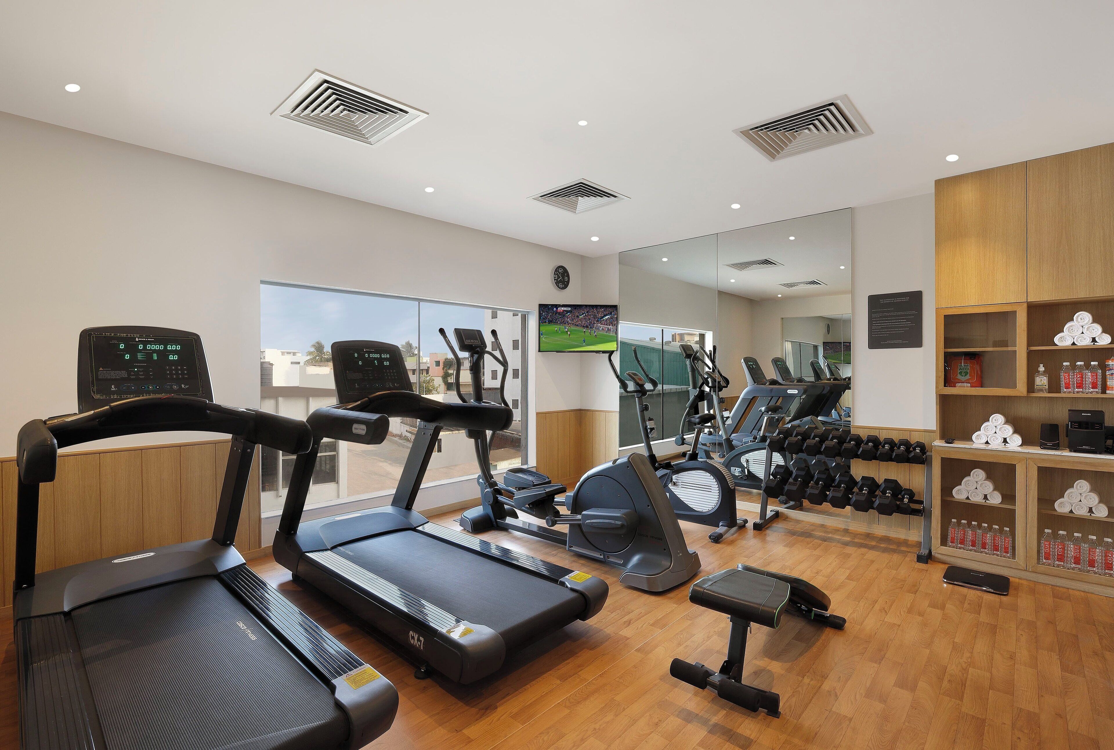 A gym with treadmills, elliptical machines, and a mirror wall.