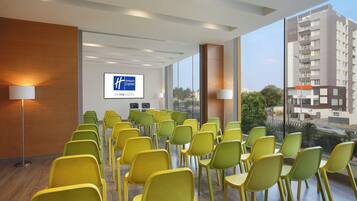 A conference room with rows of yellow chairs, a large screen displaying the Holiday Inn Express logo, and a view of a cityscape through large windows.