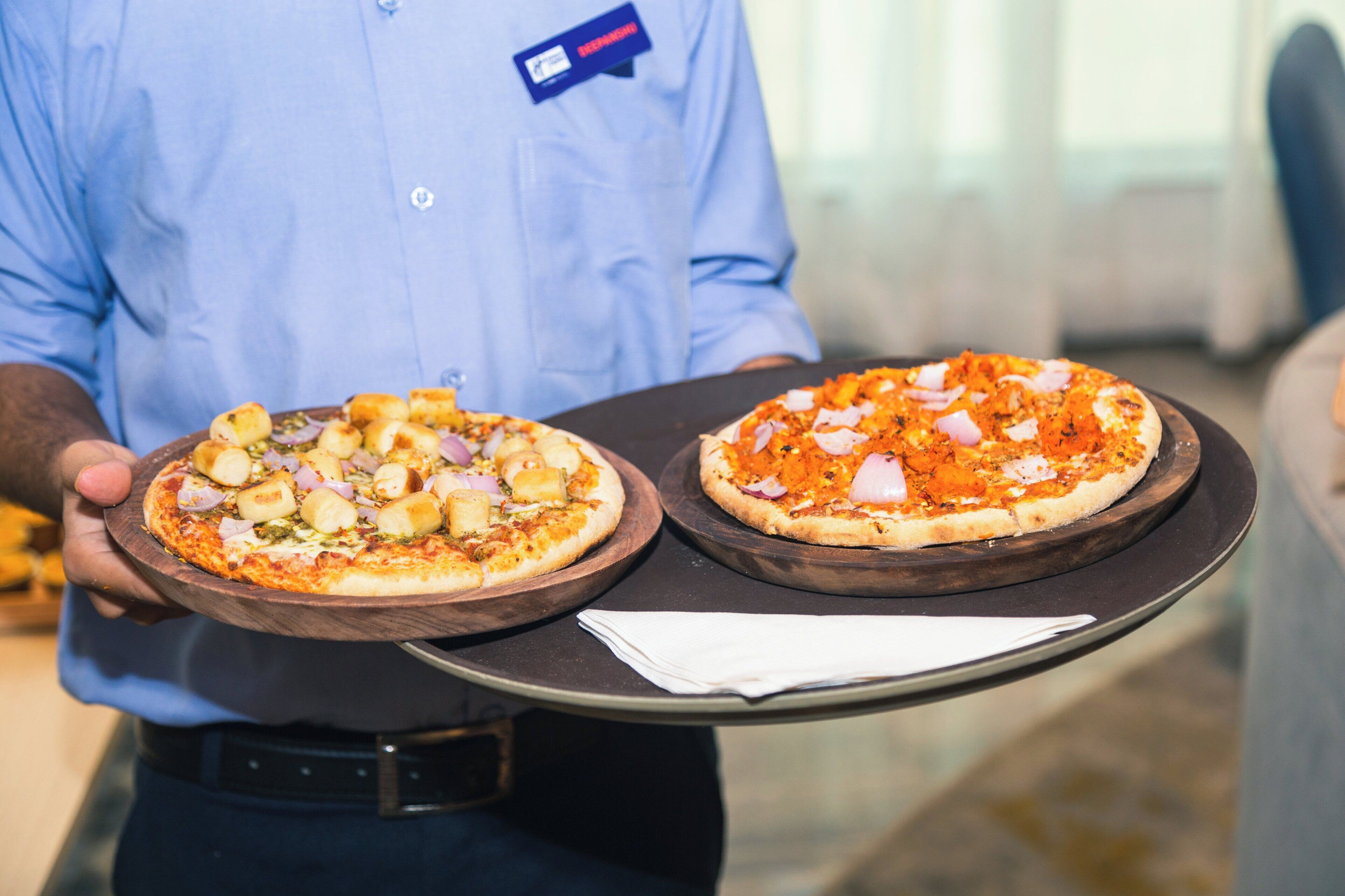 A person holding two pizzas on a wooden tray.