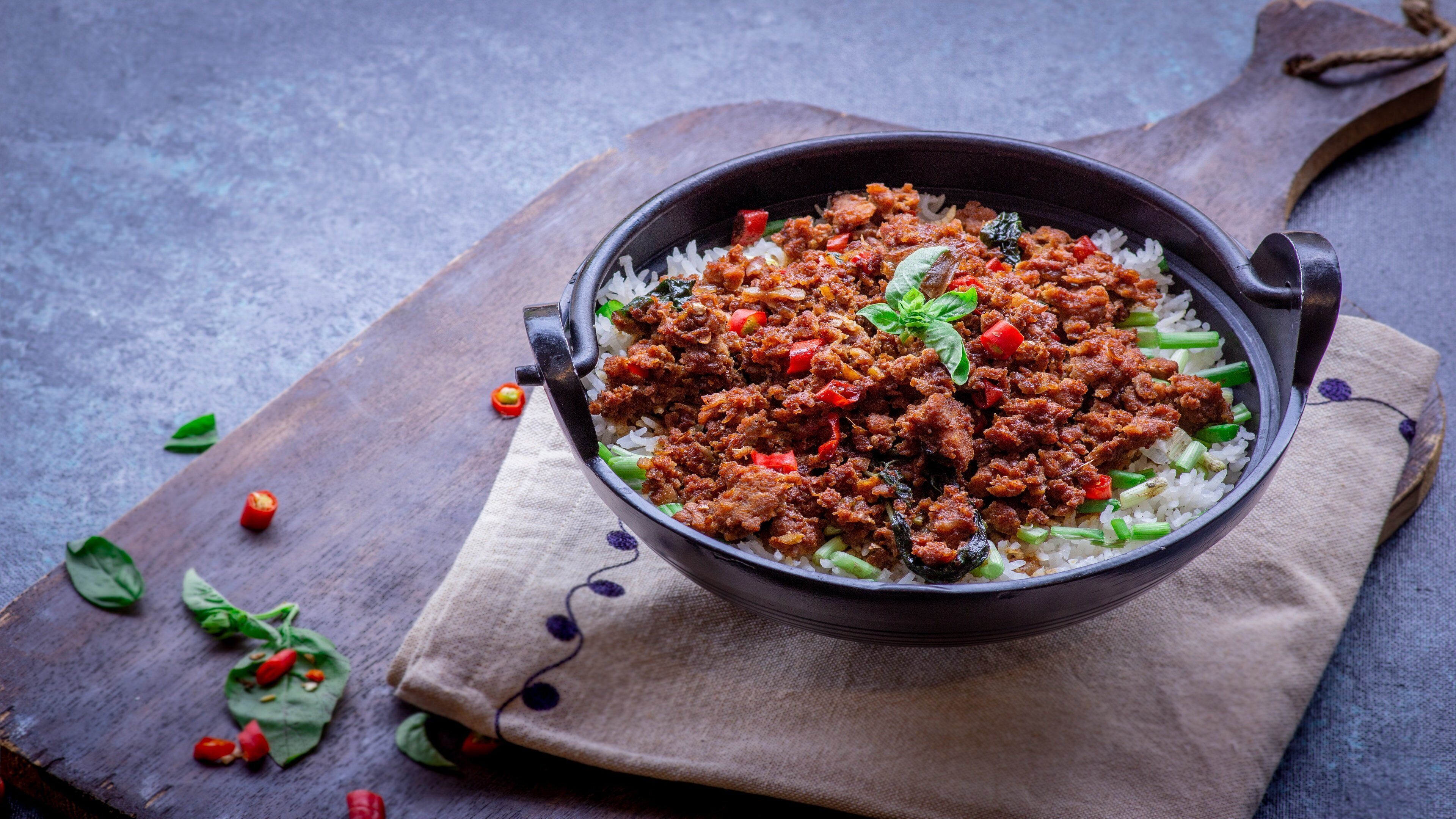 Un plato de arroz coronado con un guiso de carne, sobre una tabla de madera con un paño debajo.
