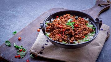 Un plato de arroz coronado con un guiso de carne, sobre una tabla de madera con un paño debajo.