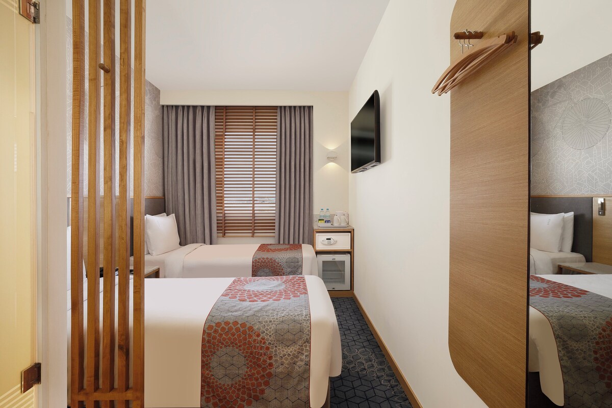 A hotel room with two beds, a desk, a TV, and a mirror.