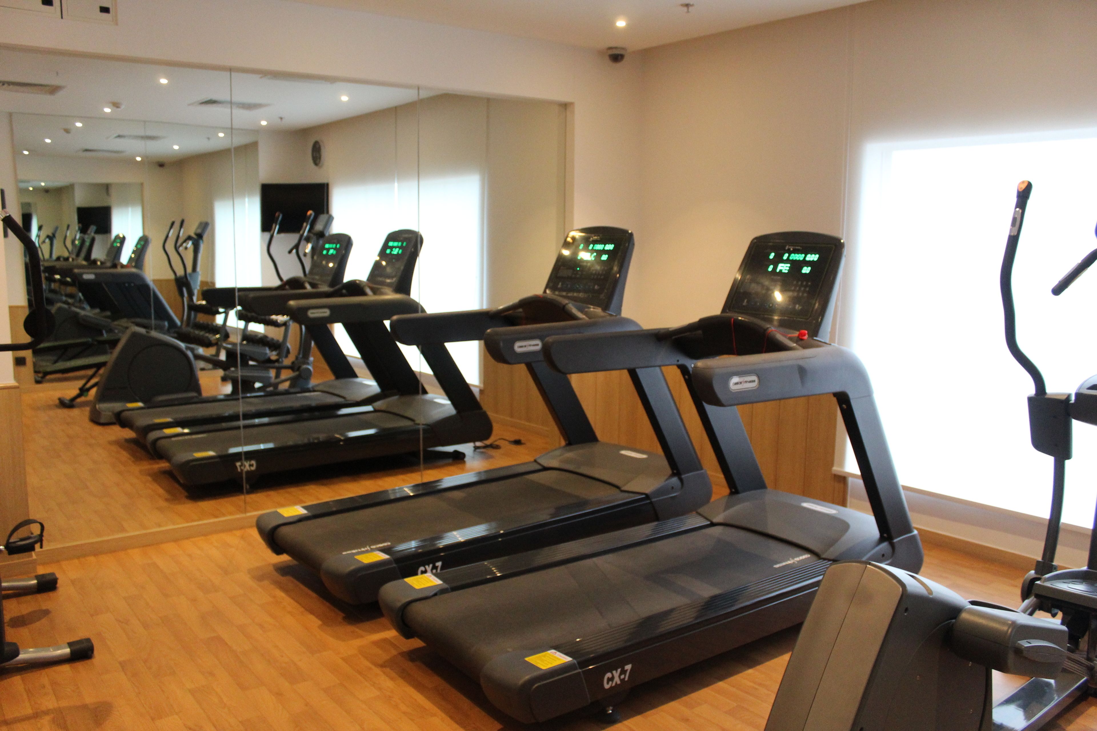 Eine Reihe von Laufbändern in einem Fitnessstudio mit Holzboden und Spiegeln an den Wänden.