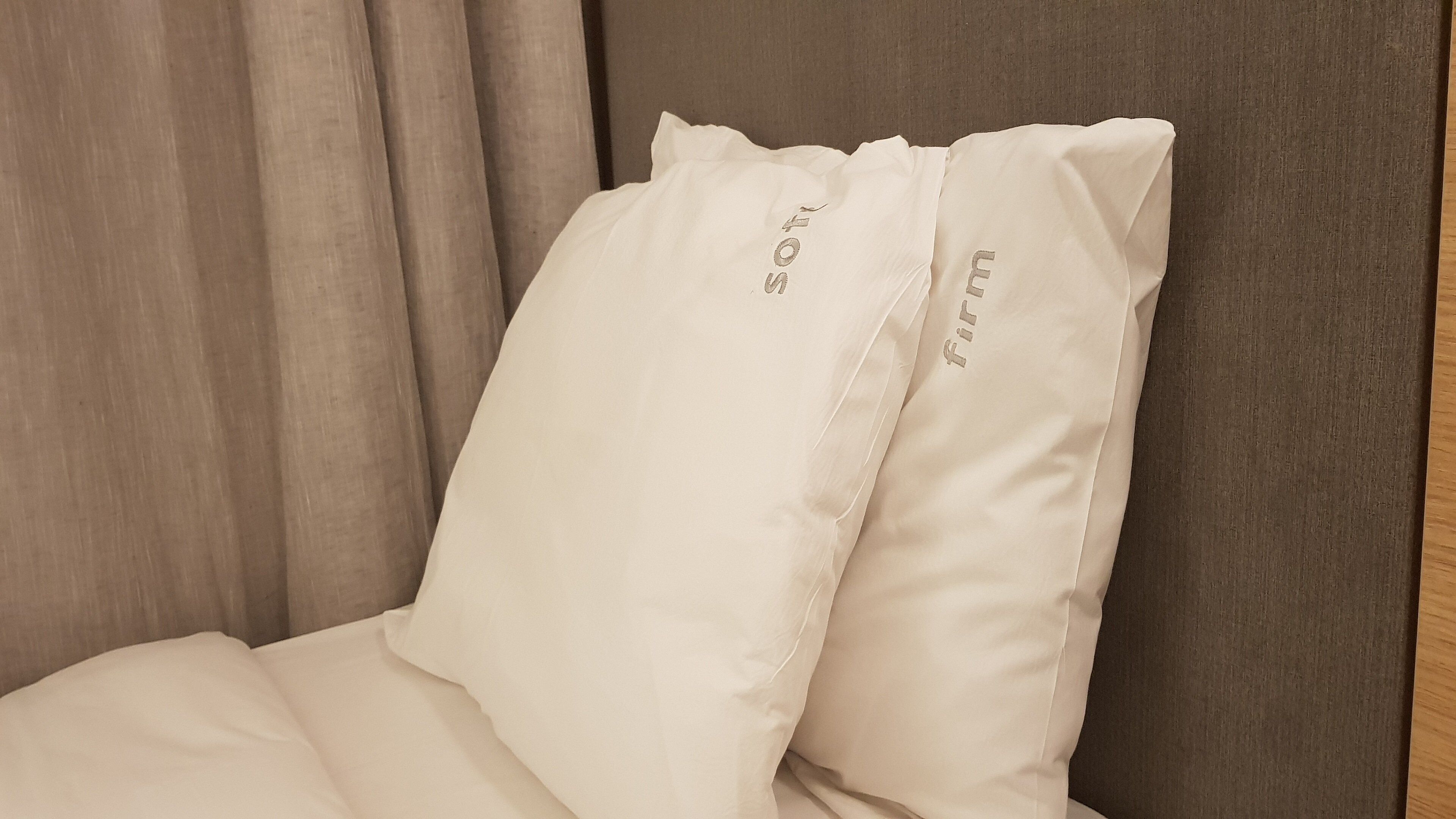A bed with two pillows, one with "SOFT" and the other with "firm" embroidered on them.