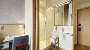 Un baño moderno con cabina de ducha de vidrio, lavamanos blanco y espejo.