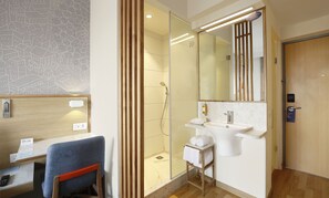 Un baño moderno con cabina de ducha de vidrio, lavamanos blanco y espejo.