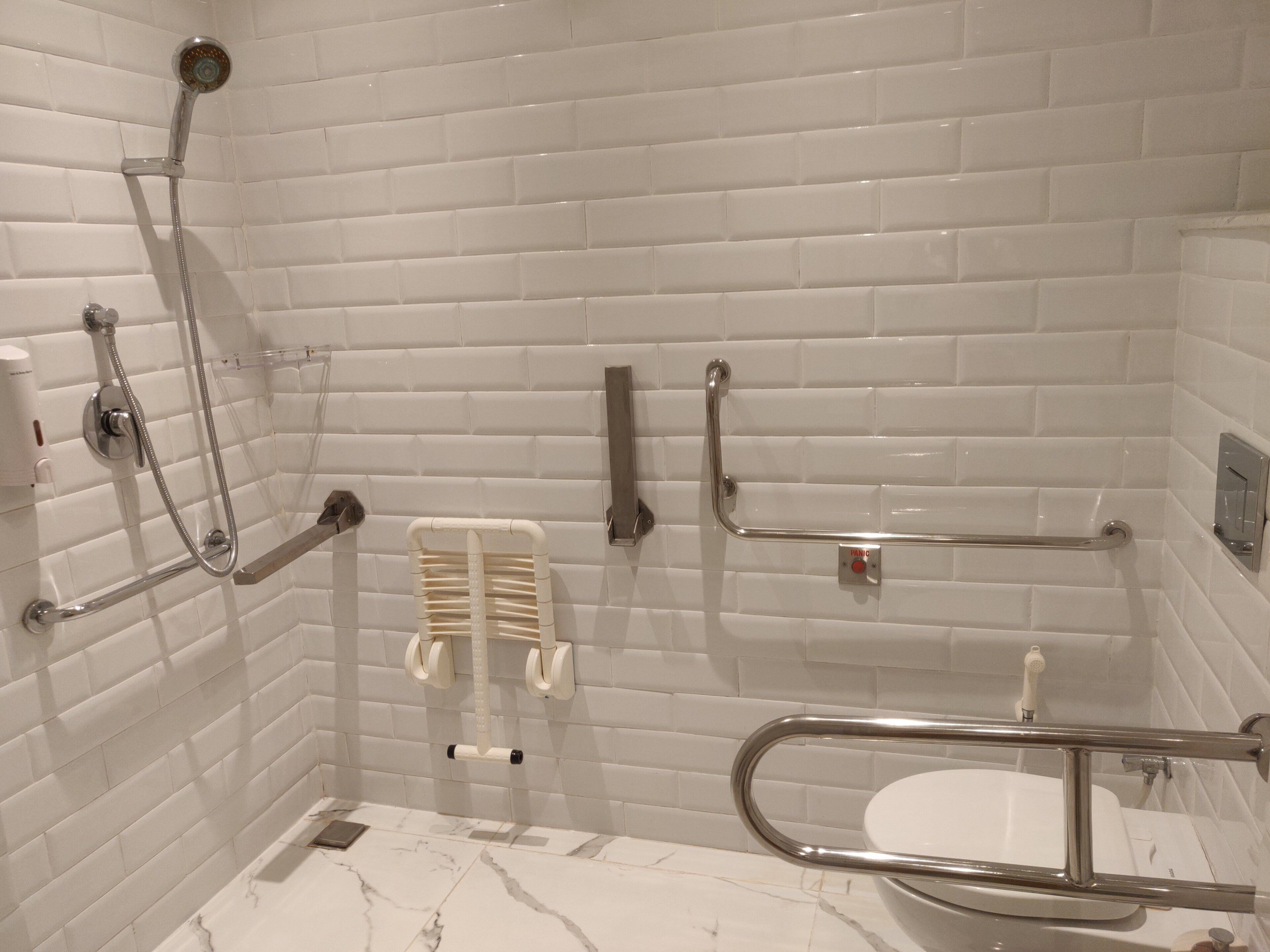 A bathroom with white subway tiles, a shower with a handheld showerhead, a grab bar, a toilet, and a sink.
