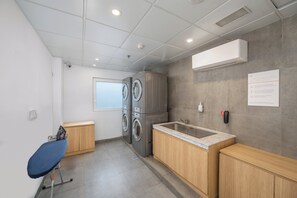 Un lavadero con lavadora, secadora, tabla de planchar y lavabo.