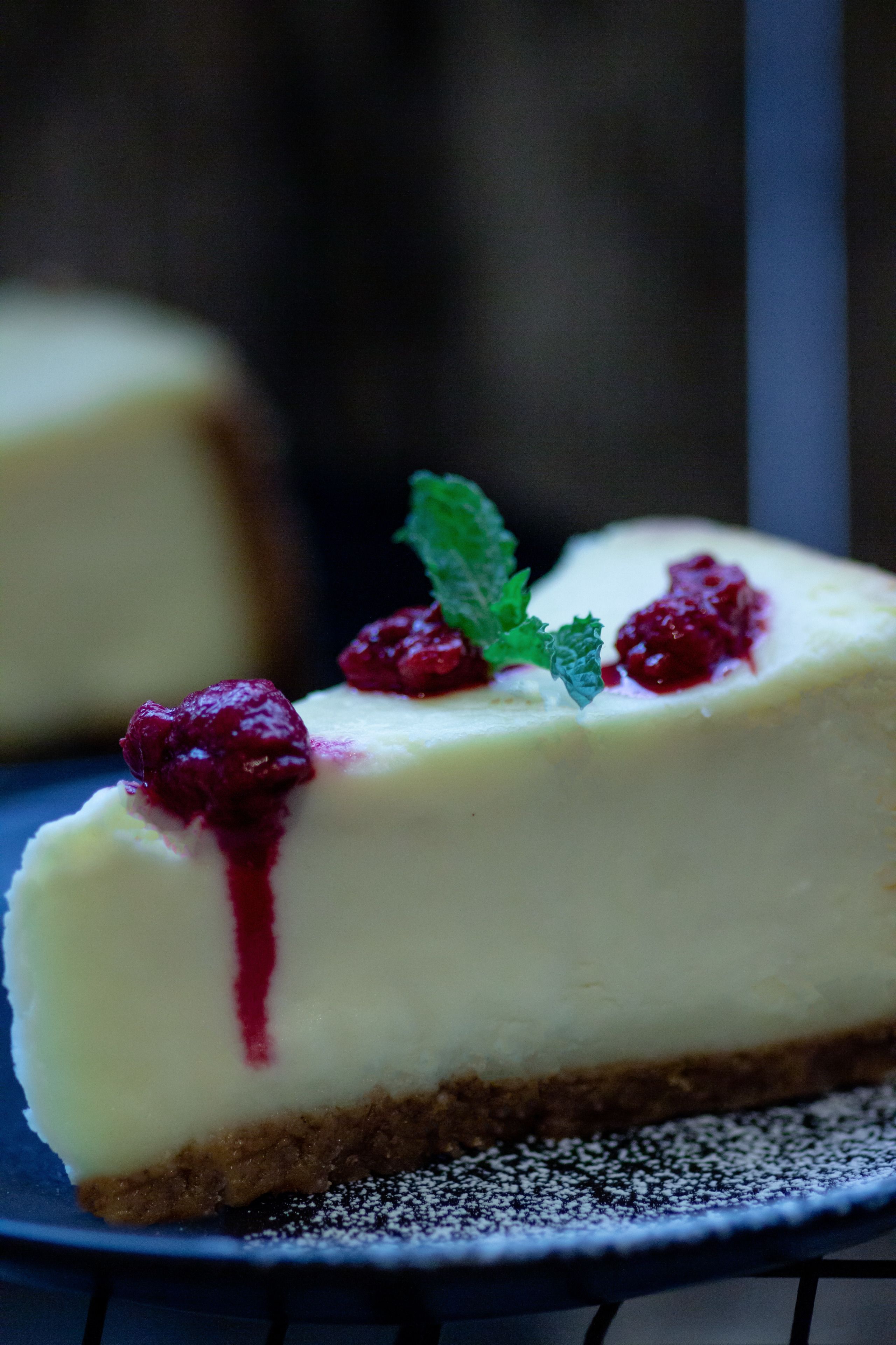 Een stuk cheesecake met bessensaus en munt.
