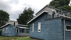 A modern blue cabin with a balcony and a covered patio area.