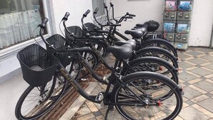 A row of bicycles parked outside a building with a tiled floor and a window with a view of trees.