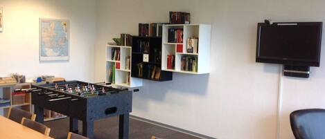 A room with a foosball table, a television, and bookshelves.