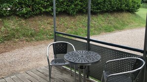 A covered outdoor seating area with metal chairs and a table, surrounded by a wooden deck and a metal railing.