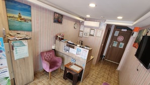 Zona de recepción con un mostrador de madera, un sillón rosa, una mesita y un televisor montado en la pared.