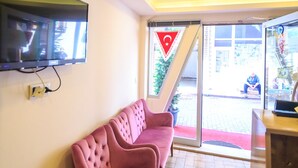 Zona de recepción con un sofá rosa, un televisor de pantalla plana en la pared y un ventanal corredero hacia el exterior.