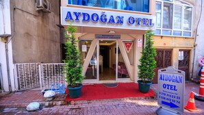 El exterior del Hotel Aydogan, con una alfombra roja en la entrada, dos plantas en macetas y un cartel con información de contacto.