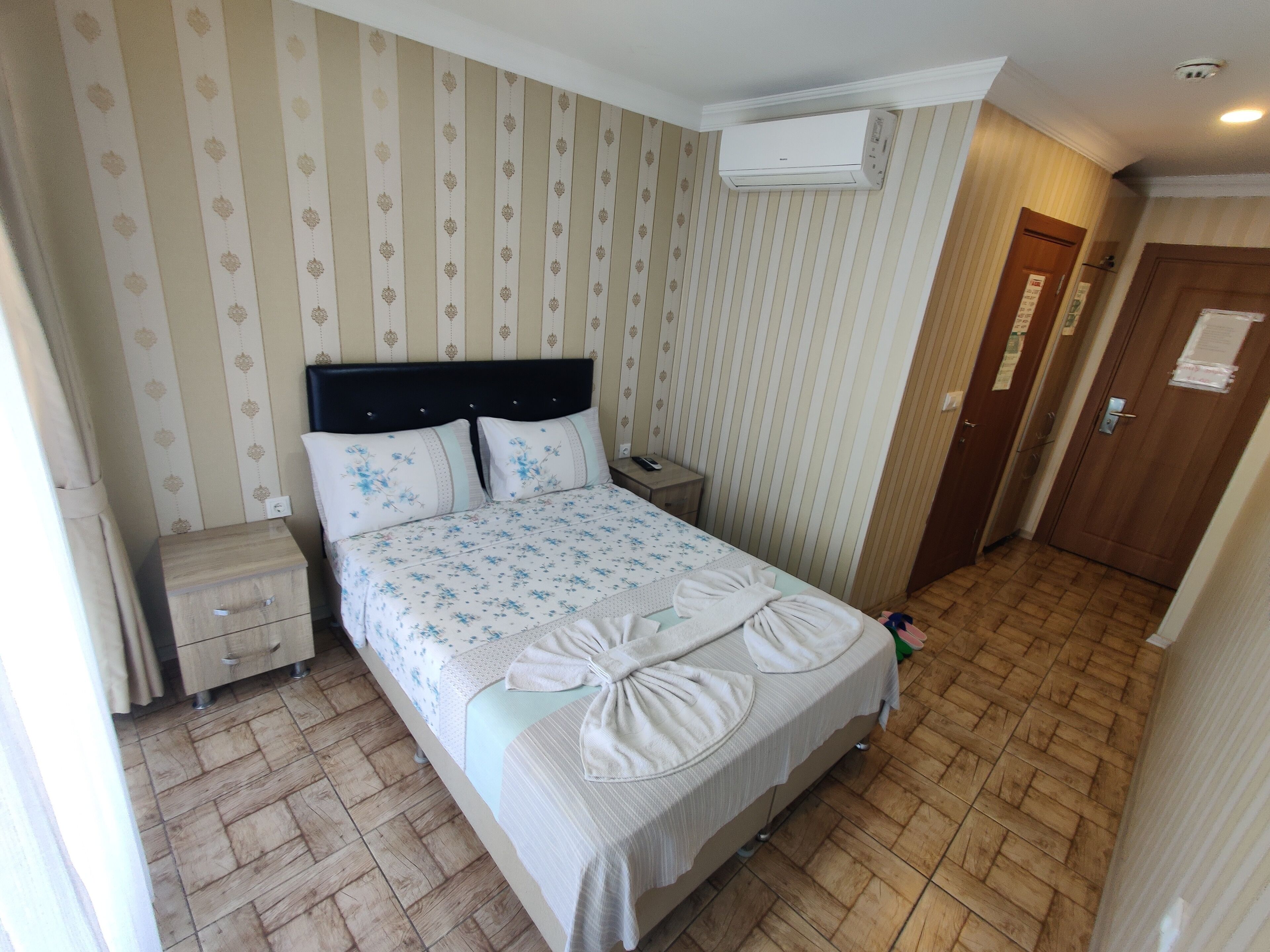 A hotel room with a bed, a nightstand, a wall-mounted air conditioner, and a door.