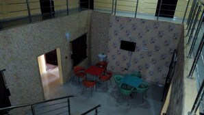 A multi-level interior with a dining area featuring red and green chairs around a table, a staircase, and a patterned wall. - Gen-Preston Hotel & Suites (Papalanto)