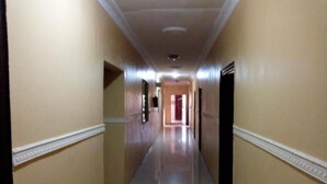 A long, narrow hallway with cream-colored walls and a shiny tiled floor. - Gen-Preston Hotel & Suites (Papalanto)