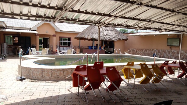 A swimming pool area with a covered roof, lounge chairs, and a thatched-roof structure. - Gen-Preston Hotel & Suites (Papalanto)