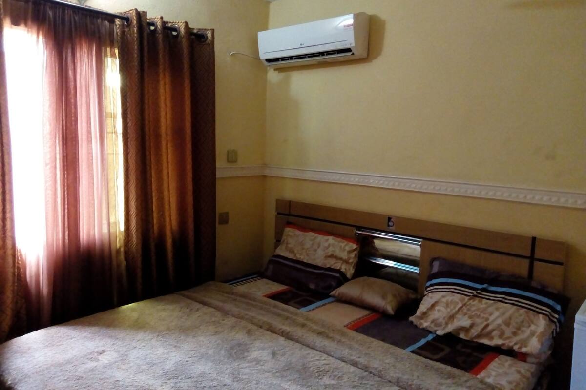 Un dormitorio con cama, cortinas, aire acondicionado e iluminación empotrada en la pared.