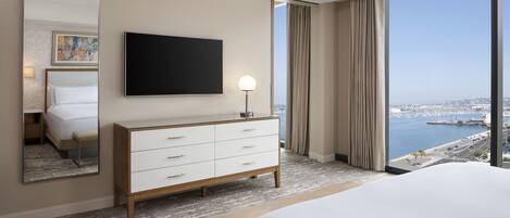 A hotel room with a large bed, a TV mounted on the wall, a dresser, and a view of the marina through large windows.