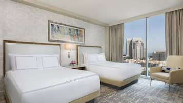 A hotel room with two beds, a large window with a city view, a painting on the wall, and a chair.