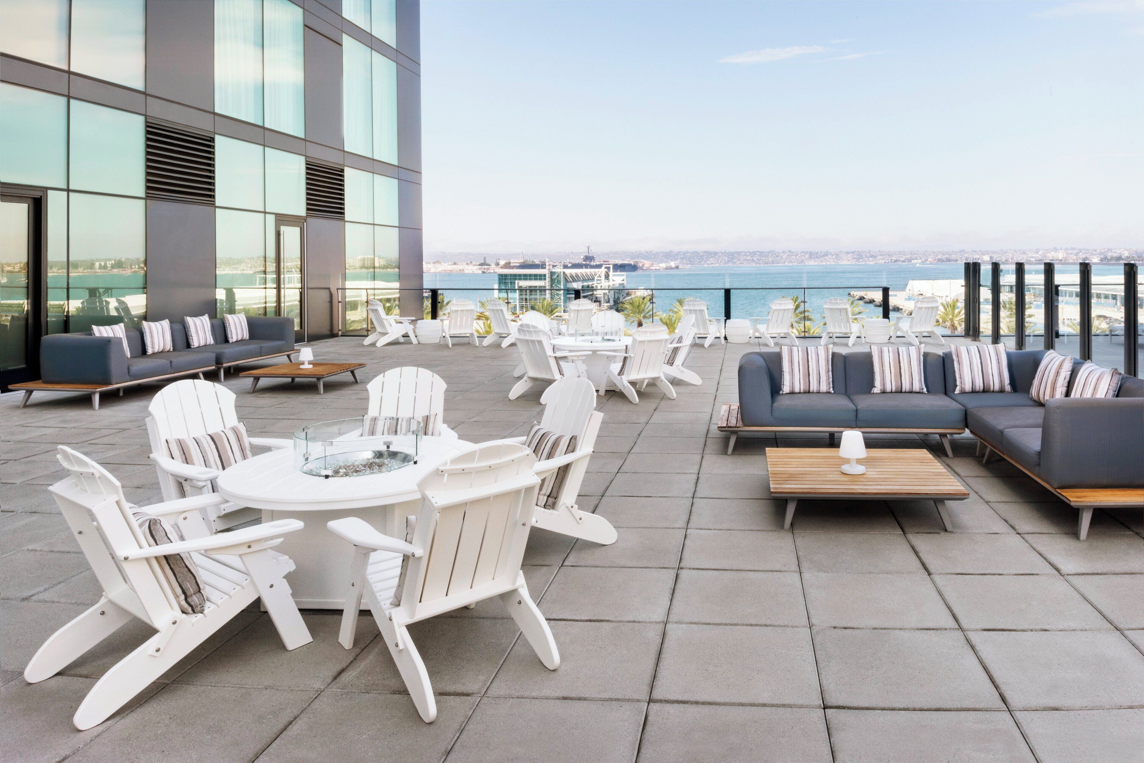 Una terraza en la azotea con mobiliario exterior, incluyendo sillas blancas y un sofá, con vista al mar.