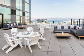 Una terraza en la azotea con mobiliario exterior, incluyendo sillas blancas y un sofá, con vista al mar.