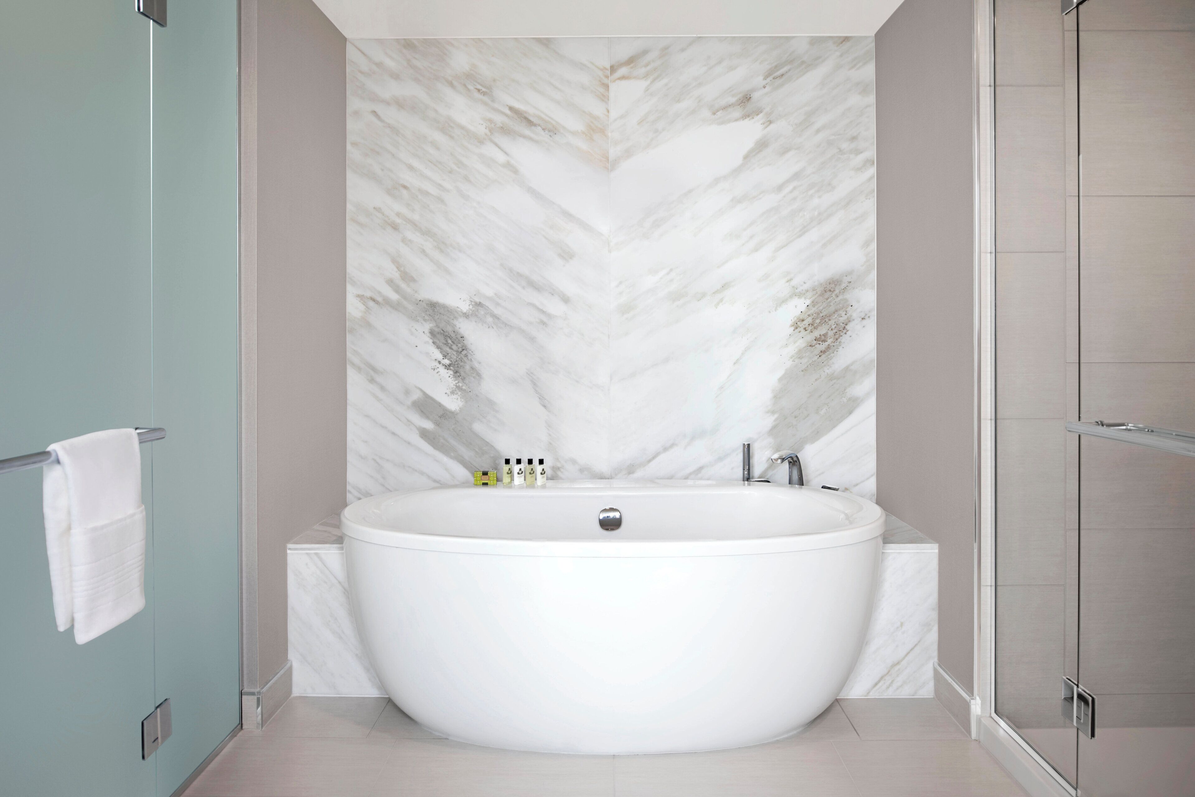 A modern bathroom with a freestanding bathtub, marble wall, and a glass shower enclosure.