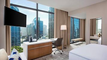 Una habitación de hotel con un ventanal grande, un escritorio, una silla, una cama y un televisor.