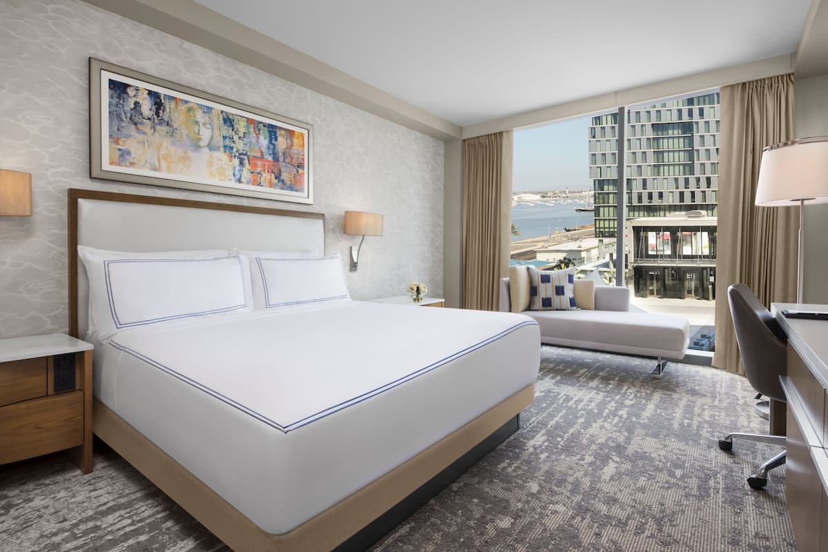 A hotel room with a large bed, a desk, a chair, a sofa, and a view of the city and sea.