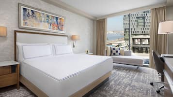 A hotel room with a large bed, a desk, a chair, a sofa, and a view of the city and sea.