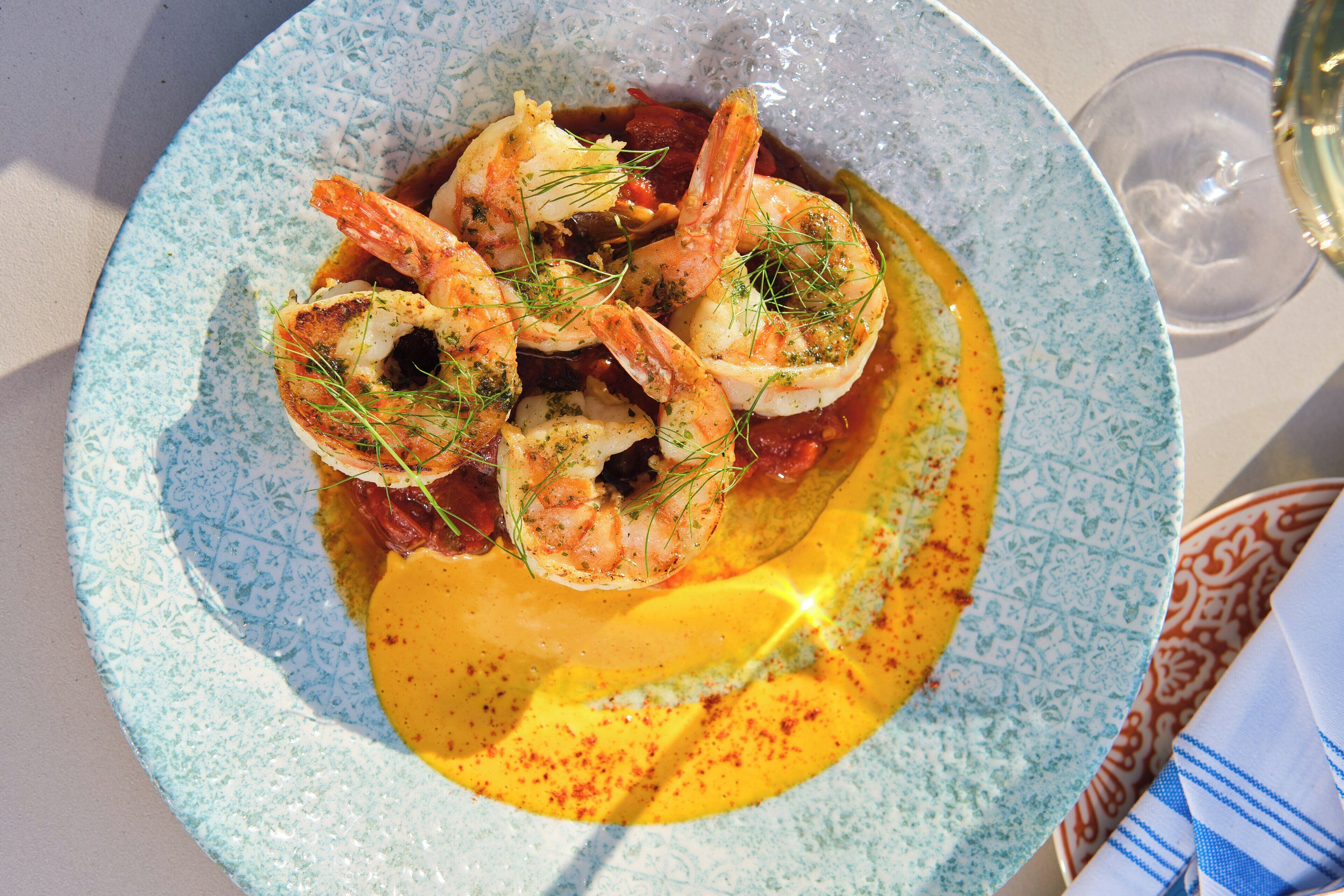 A plate of shrimp with a yellow sauce, garnished with herbs, on a patterned plate.