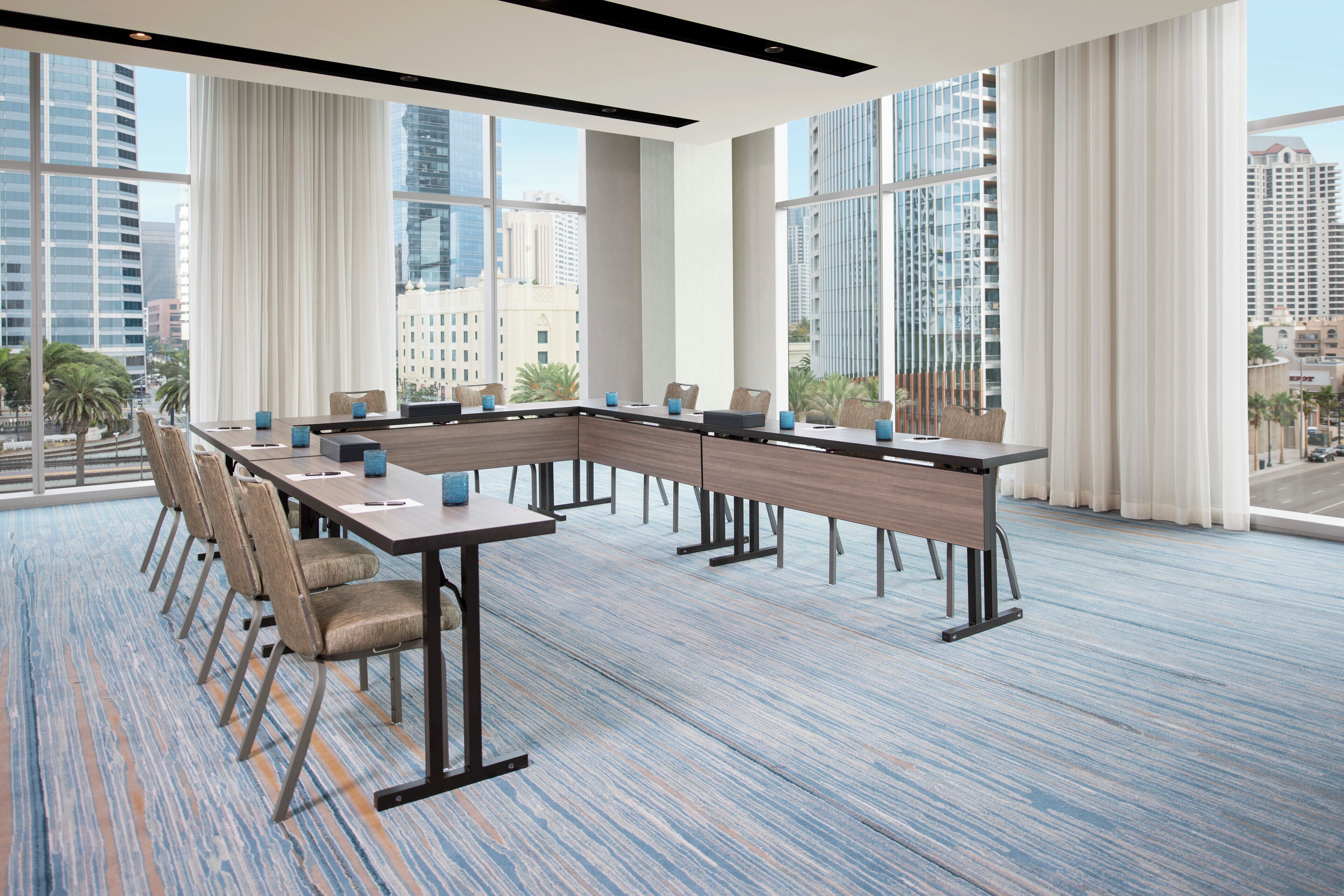 A conference room with a long table, chairs, and large windows offering city views.