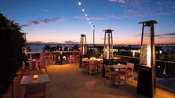 Une terrasse extérieure avec des tables et des chaises, des guirlandes lumineuses et une vue sur les toits de la ville au crépuscule.