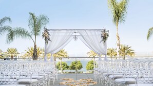 A wedding aisle with white chairs and a floral arch, overlooking a scenic view.