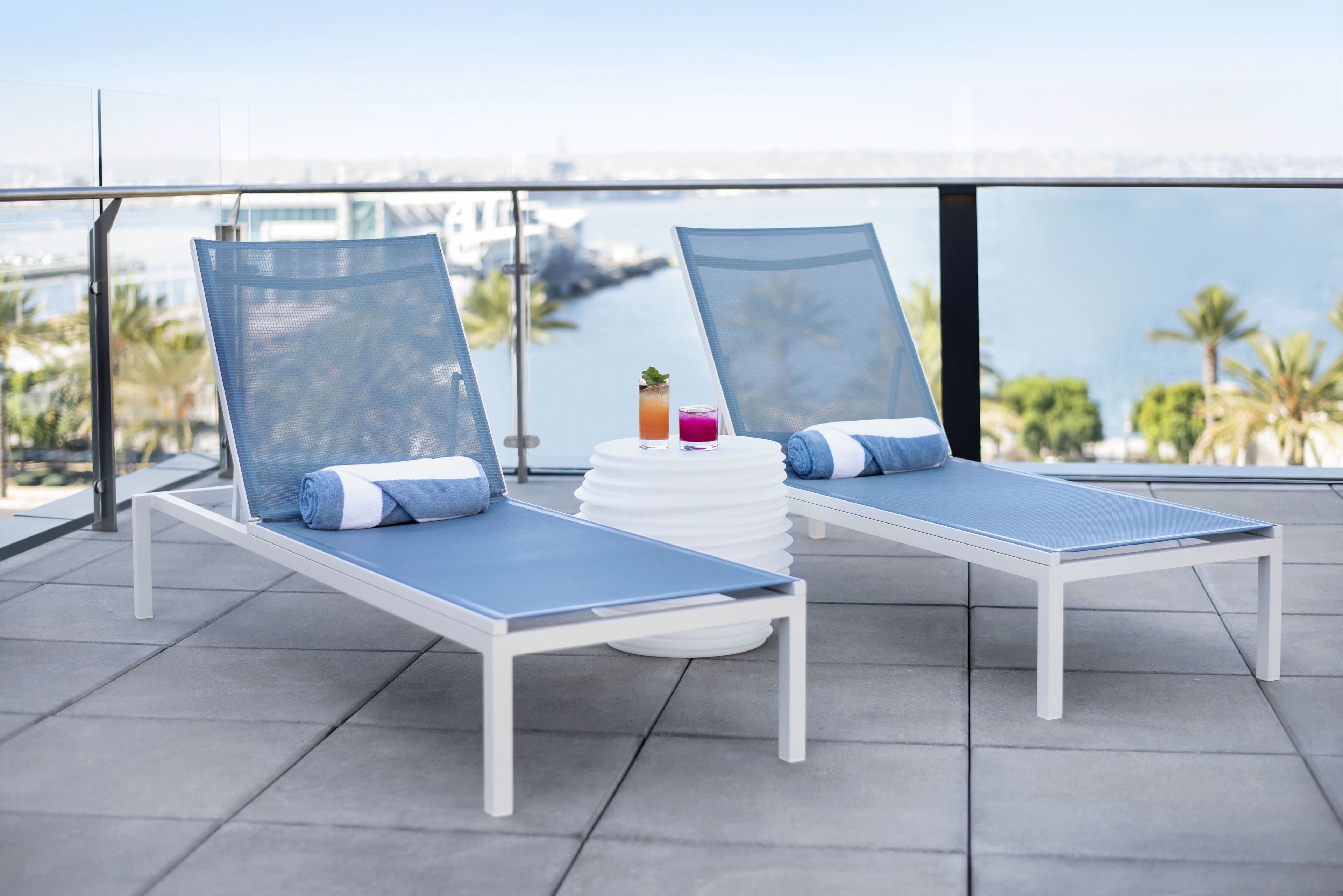 Two lounge chairs with blue cushions and a white table with drinks and a small plant.