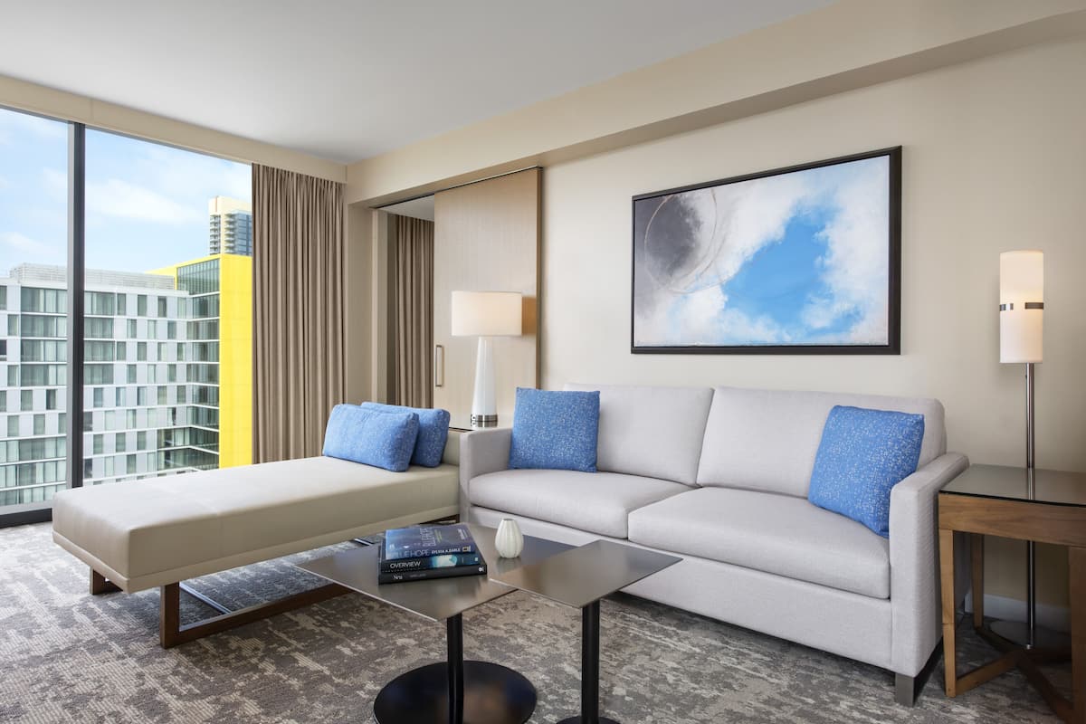 A modern hotel room with a sofa, a coffee table, a lamp, and a painting.